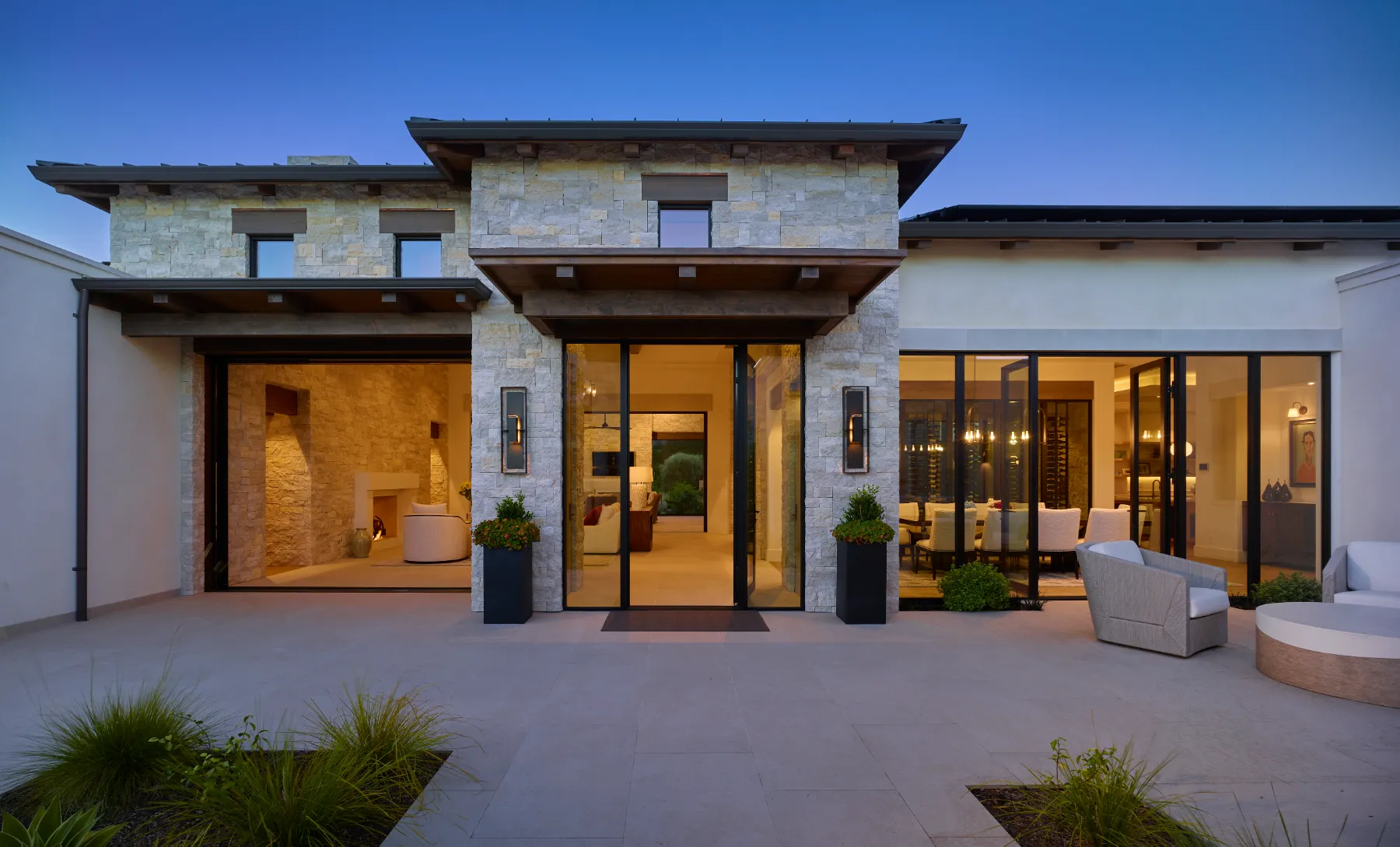 Stone entry court of a custom home at dusk, lit from within
